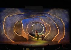 two people standing on stage in front of an artisticly designed tunnel with lights at the end