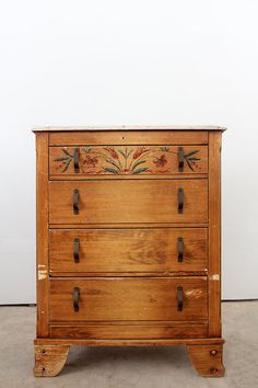 an old wooden dresser with floral designs on it's drawers and handles, in front of a white wall