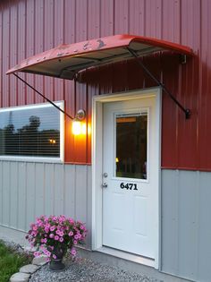 an umbrella is hanging over the door of a red building with pink flowers in front