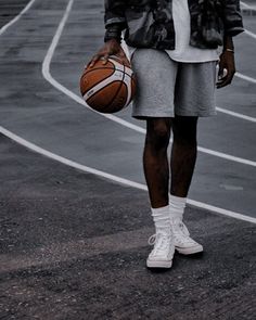 a man holding a basketball while standing on top of a basketball court with his hands in his pockets