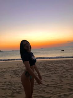 a woman standing on top of a sandy beach next to the ocean with her leg in the air