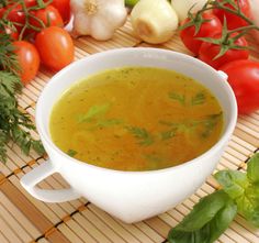 a bowl of soup sits on a bamboo mat surrounded by fresh vegetables and carrots