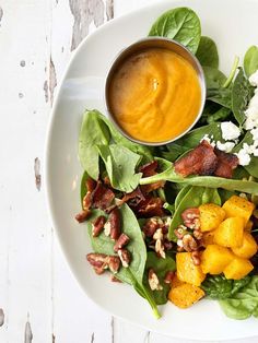 a white plate topped with spinach and bacon next to a bowl of orange sauce