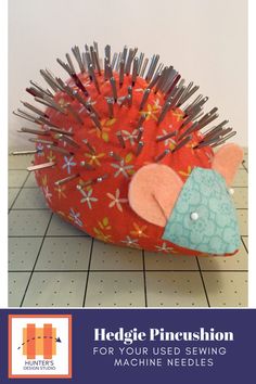 a red hedgehog pincushion sitting on top of a tiled floor