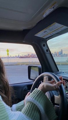 the woman is driving her car on the road in front of the cityscape