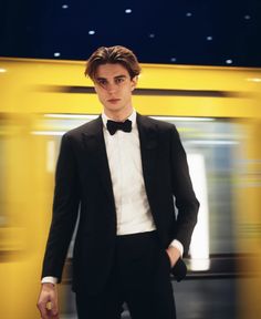 a young man in a tuxedo and bow tie standing next to a train