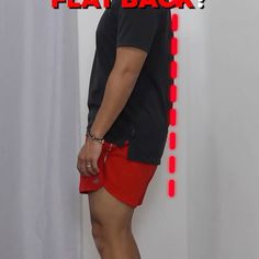 a man in black shirt and red shorts standing next to white wall with text over it