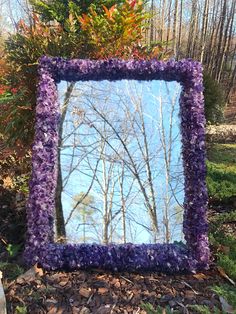 a mirror that is sitting on the ground in front of some bushes and trees with purple flowers