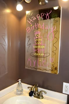 a bathroom sink sitting under a mirror with writing on the wall behind it and lights above it