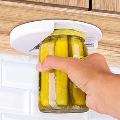 a person holding a jar with pickles in it on the kitchen counter top next to a drawer