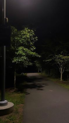 a street light on the side of a road at night with trees in the background