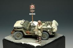 a toy soldier standing next to an army vehicle with a sign in the back ground