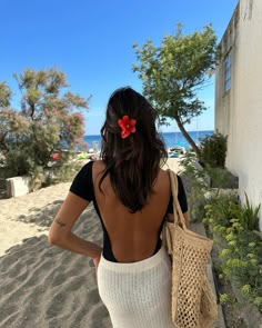 a woman with a red flower in her hair is walking on the sand towards the ocean