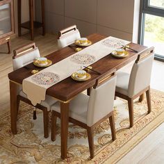 a dining room table with white chairs and plates on the placemat, in front of a large window