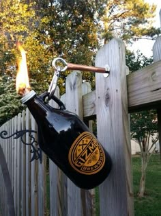 a beer bottle hanging from the side of a wooden fence with a lighter attached to it