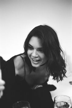 black and white photograph of a woman smiling with two wine glasses in front of her