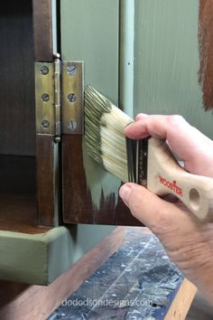 a person holding a paint brush in front of a wooden cabinet with the door open