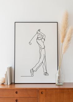 a black and white drawing of a woman playing golf on a wall above a dresser