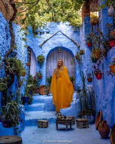 a woman standing in an alleyway with blue walls and potted plants on either side