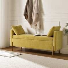 a yellow bench sitting on top of a wooden floor next to a white rug and coat rack