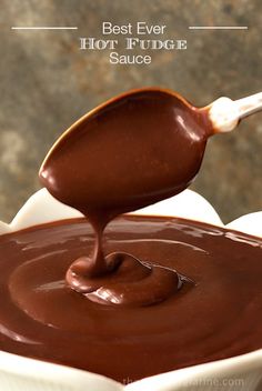 a spoon full of melted chocolate on top of a white bowl filled with liquid and sauce