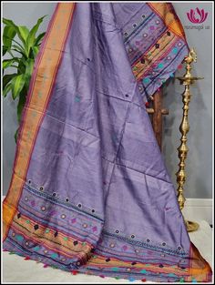 a purple and orange sari with colorful designs on the border, sitting next to a potted plant