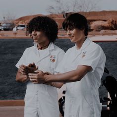 two young men in white uniforms standing next to each other with their hands together and looking at something on the ground