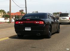 the back end of a black car driving down a street next to other cars and palm trees