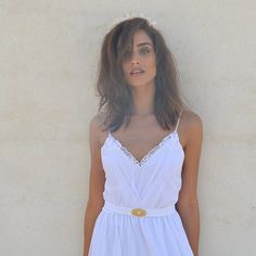 a woman standing in front of a wall wearing a white dress with gold buttons on it