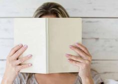 a woman is hiding her face behind a book