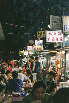 many people are sitting at tables in front of the food stand on the side of the street