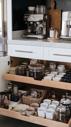 an open drawer in a kitchen filled with cups and saucers next to a coffee maker