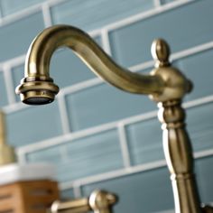 a gold faucet in front of a blue brick wall with white tiles on it