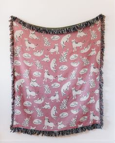 a pink wall hanging with white dogs on it and fringe trimming around the edges