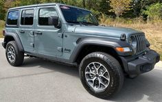 a gray jeep is parked on the side of the road in front of some trees