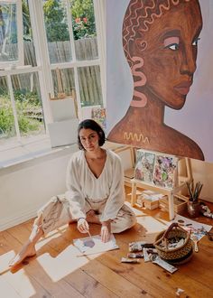 a woman sitting on the floor in front of a painting