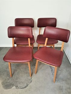 four red leather chairs sitting next to each other in a room with concrete flooring