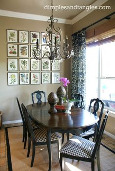 a dinning room table with chairs and pictures on the wall behind it in front of a window