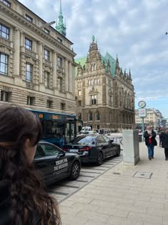 a woman standing on the sidewalk in front of a bus and some buildings with people walking by