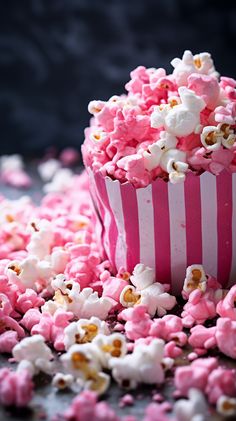 pink and white popcorn is spilled out of a striped paper cup onto the ground,