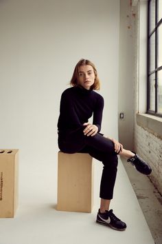 a woman sitting on top of a wooden block next to a box in an empty room