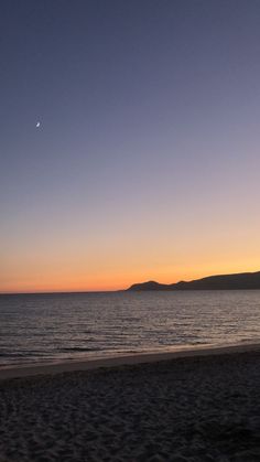 the sun is setting at the beach with mountains in the distance and water on the shore