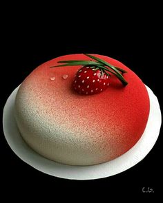 a red and white cake on a plate with a strawberry sitting on top of it