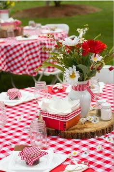 a table set with red and white checkered tables cloths, plates, cups, vases and utensils