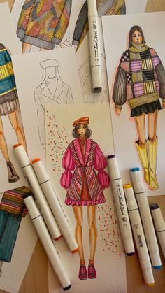 fashion sketches and markers are laid out on the table