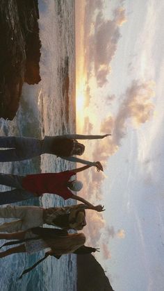 four people standing in front of the ocean at sunset