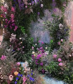 a garden filled with lots of flowers next to a pink wall covered in greenery