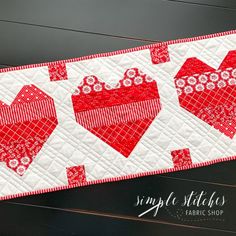 a red and white quilted table runner with two hearts on it, along with the words simply stitches fabric shop