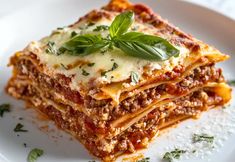 a white plate topped with lasagna covered in sauce and cheese, garnished with green leaves