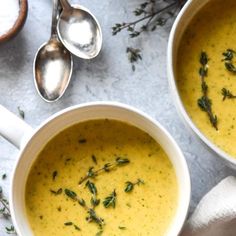 two white bowls filled with soup next to spoons on a gray tablecloth and silverware